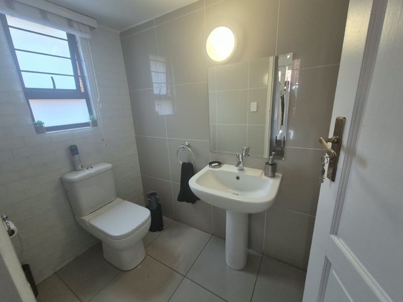 A clean and functional bathroom featuring a pedestal basin, toilet, and neutral wall tiling with a window for natural light.