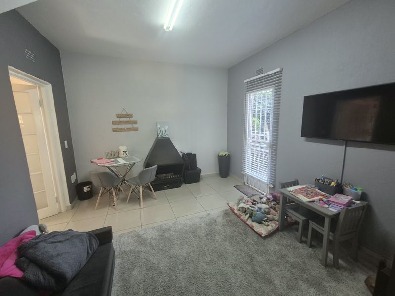 A living room featuring tiled flooring, a freestanding fireplace, and natural light through a window with venetian blinds.