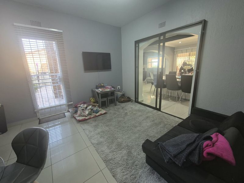 A living room featuring tiled flooring, a sliding glass door leading to an adjacent dining area, and venetian blinds.