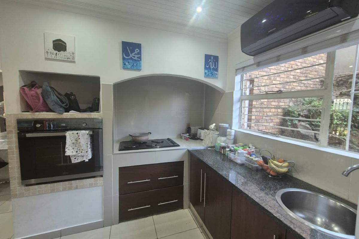A functional kitchen featuring granite countertops, built-in oven, gas hob, and dark wood cabinetry, complemented by tiled flooring and a wall-mounted air conditioning unit.