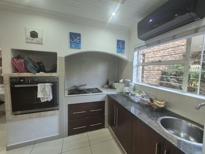 A functional kitchen featuring granite countertops, built-in oven, gas hob, and dark wood cabinetry, complemented by tiled flooring and a wall-mounted air conditioning unit.