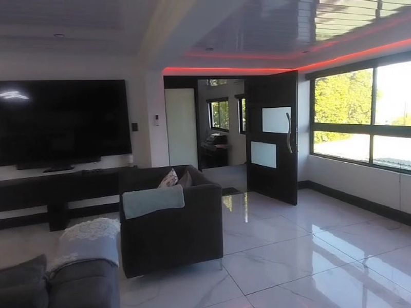 A modern living room featuring polished porcelain tile flooring, recessed ceiling lighting with integrated LED accents, and large windows providing ample natural light.