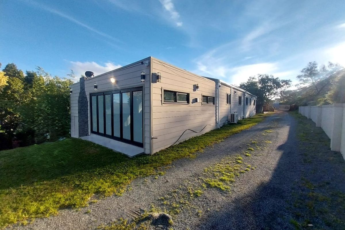 Rear view of the property featuring modern horizontal cladding, bi-fold doors, a stone chimney, and a gravel driveway.