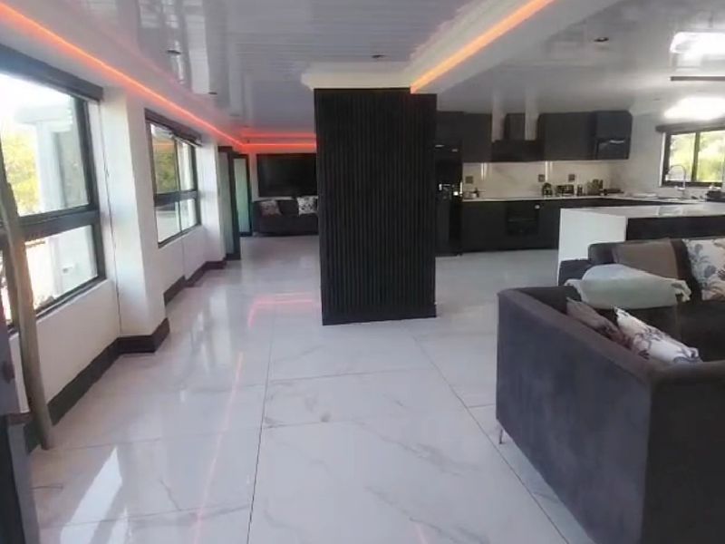 Modern open-plan living area featuring high-gloss marble-look flooring, recessed ambient lighting, a central slatted feature column, and a sleek contemporary kitchen.