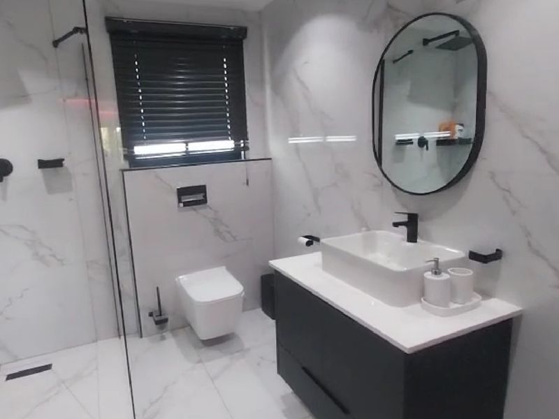 Modern bathroom featuring marble-look wall tiles, a sleek vanity with vessel sink, wall-mounted toilet, and a spacious walk-in shower with black matte fixtures.