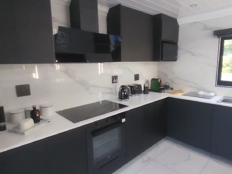 Modern kitchen featuring matte black cabinetry, white marble-look countertops and splashbacks, integrated appliances, and a sleek undermount sink with a gooseneck faucet.