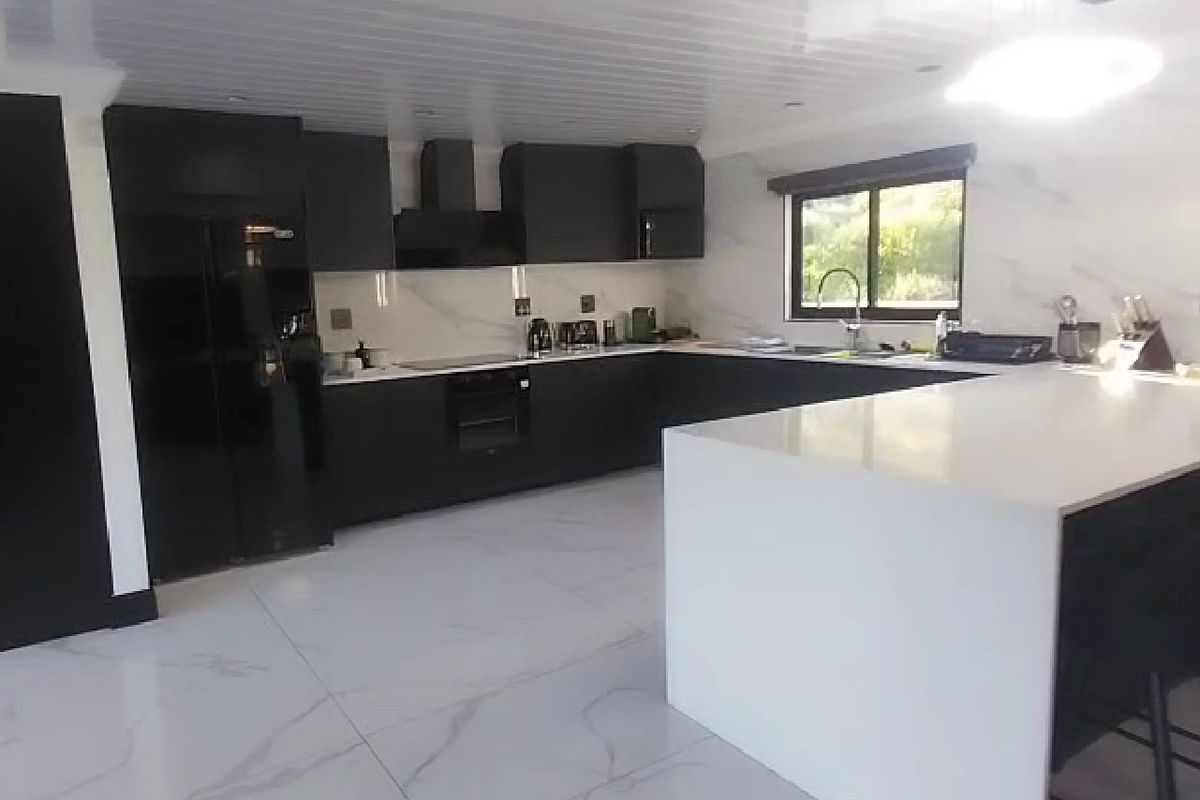 Modern kitchen featuring sleek black cabinetry, white stone countertops, a large central island, and high-end marble-look flooring and backsplash.