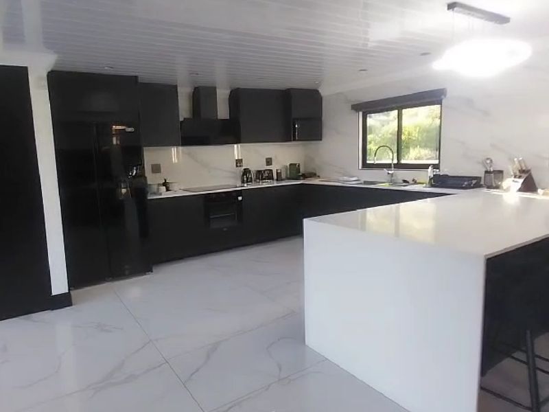 Modern kitchen featuring sleek black cabinetry, white stone countertops, a large central island, and high-end marble-look flooring and backsplash.