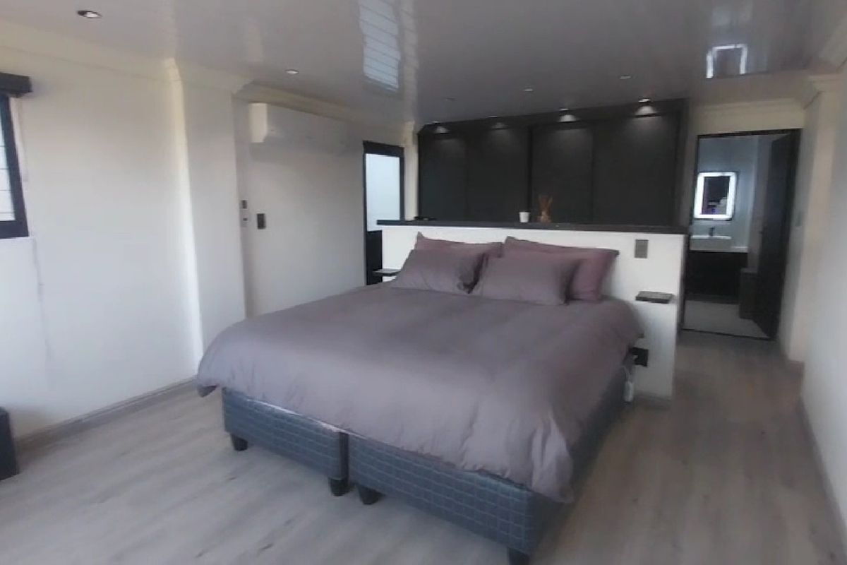 Modern bedroom featuring laminate flooring, recessed lighting, a split-system air conditioner, and built-in cupboards with direct access to an en-suite bathroom.