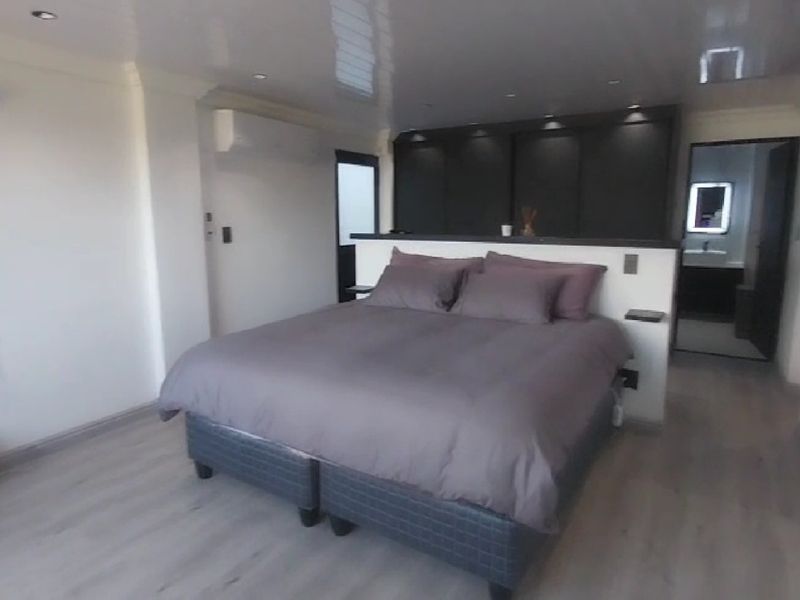 Modern bedroom featuring laminate flooring, recessed lighting, a split-system air conditioner, and built-in cupboards with direct access to an en-suite bathroom.