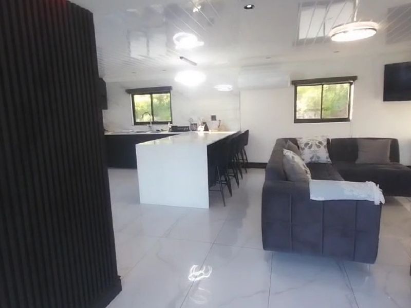 Modern open-plan living area featuring a sleek kitchen island, glossy tiled flooring, and contemporary slatted wall accents.
