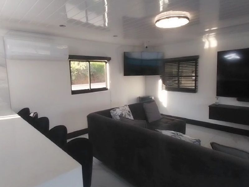 A modern living room featuring tiled flooring, recessed lighting, a wall-mounted television, and a split-system air conditioner.