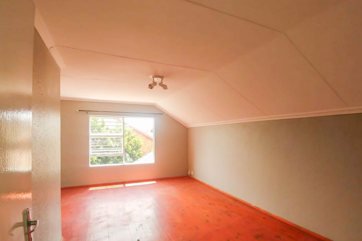 An empty bedroom featuring sloped ceilings, timber flooring, and a window with security bars, offering a blank canvas for potential interior design.