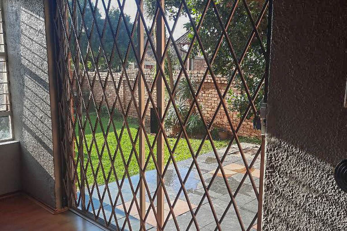Empty living area featuring laminate flooring and a sliding glass door with an integrated security gate, providing direct access to the rear garden.