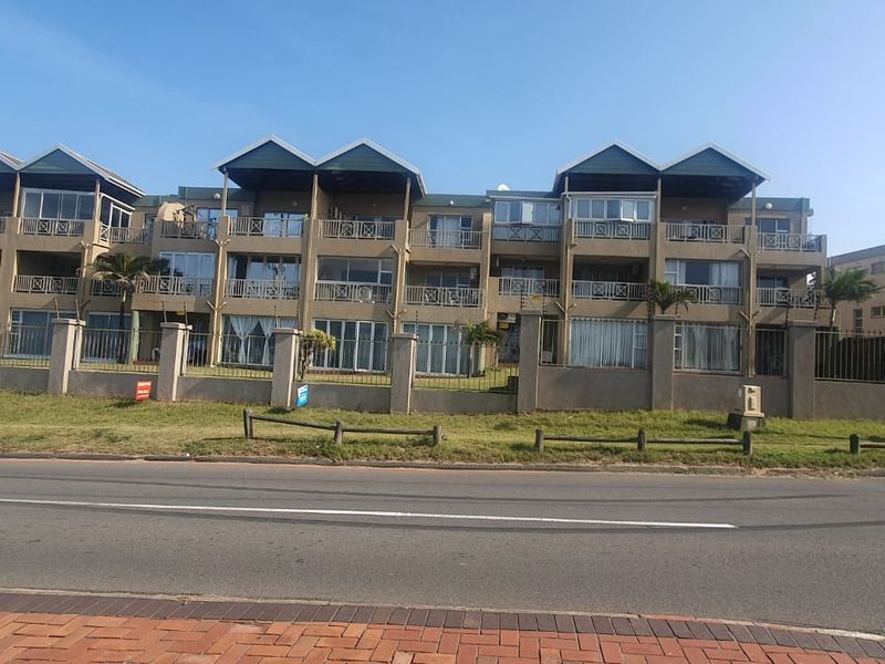 Front elevation of a multi-story apartment complex featuring balconies, sliding doors, and secure perimeter fencing.