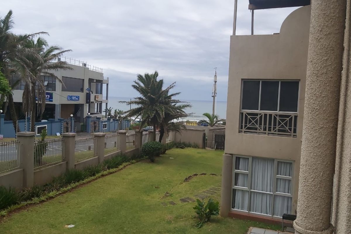 Rear view of the apartment building featuring a landscaped lawn, perimeter fencing, and balcony access with views toward the ocean.