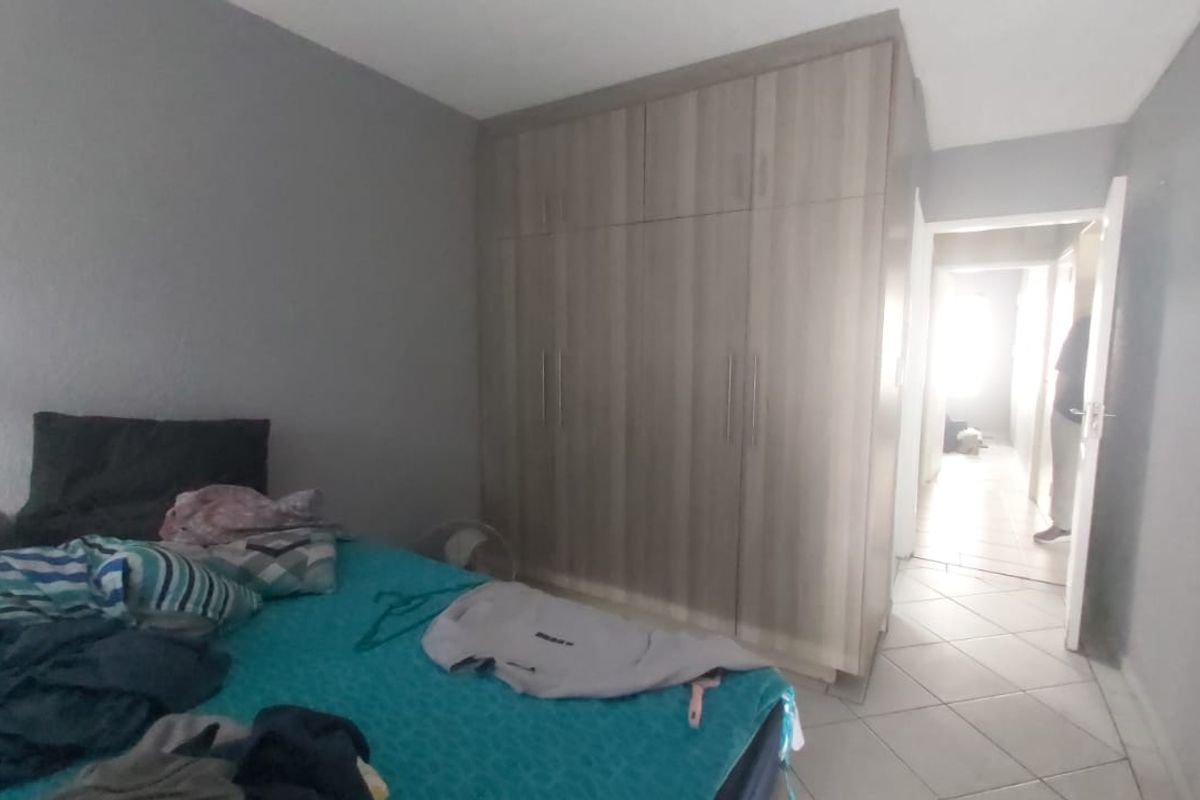 A bedroom featuring built-in wooden wardrobes and tiled flooring, with a doorway leading to a hallway.