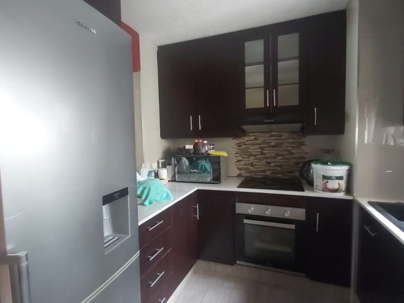 A functional kitchen featuring dark wood cabinetry, a built-in oven with hob, mosaic tile backsplash, and a modern sink area.