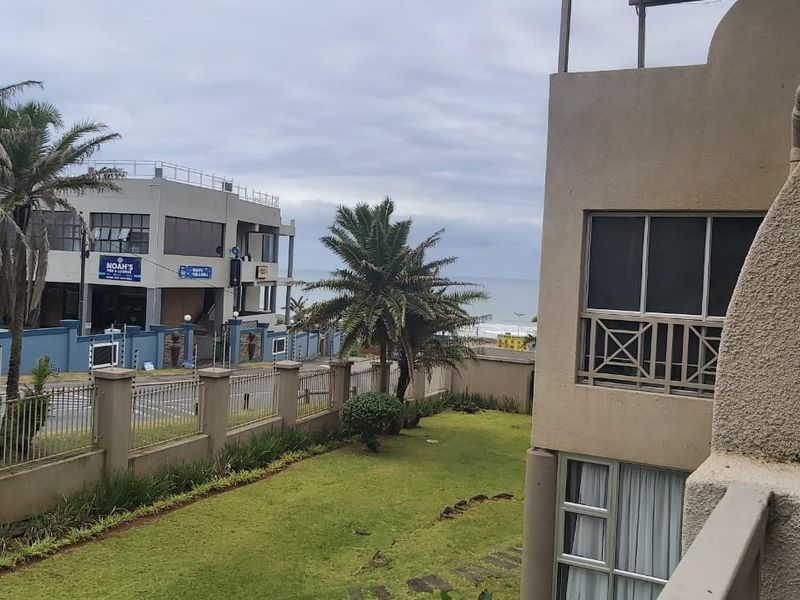 View from the apartment balcony overlooking the garden, perimeter wall, and nearby coastal streetscape.