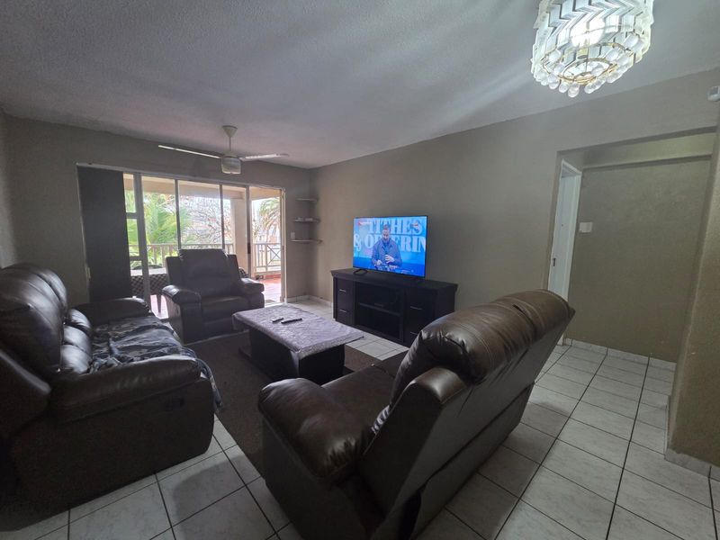 A spacious living room featuring tiled flooring, a ceiling fan, and large sliding glass doors that provide access to an outdoor balcony area.