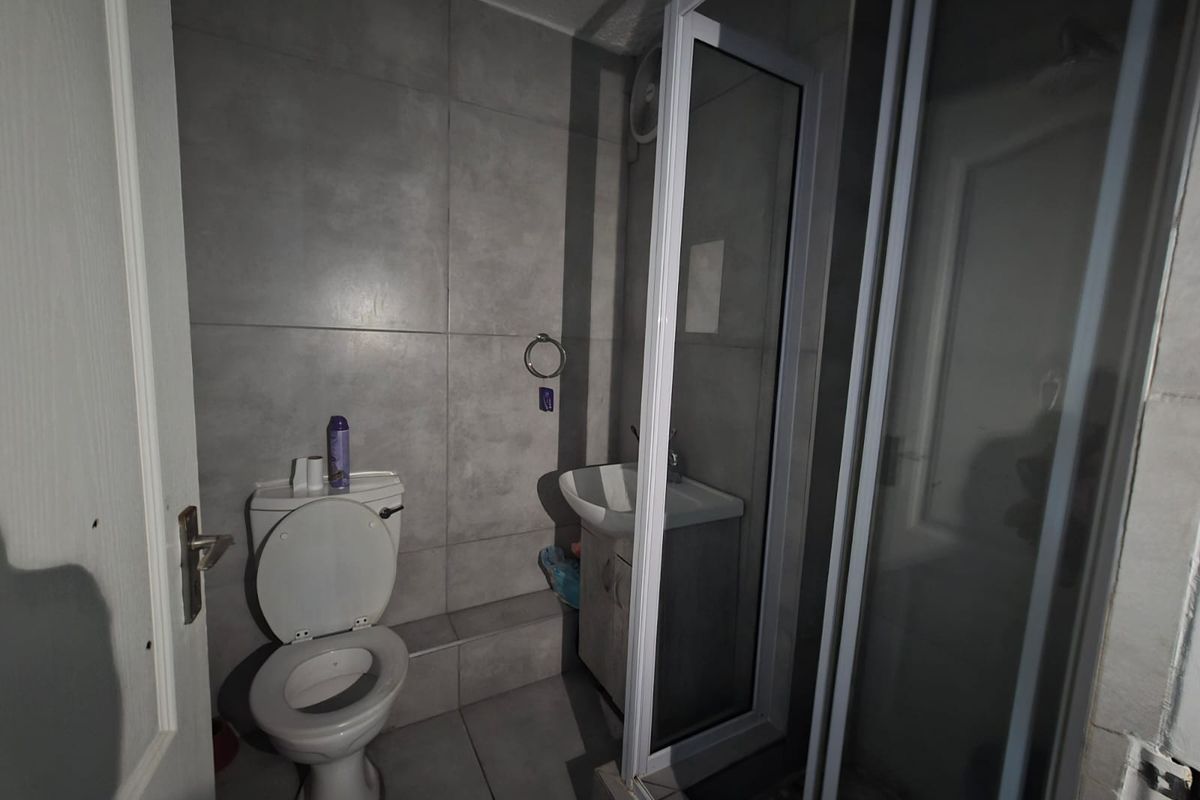A compact bathroom featuring grey wall and floor tiles, a vanity basin, a toilet, and a glass-enclosed shower unit.