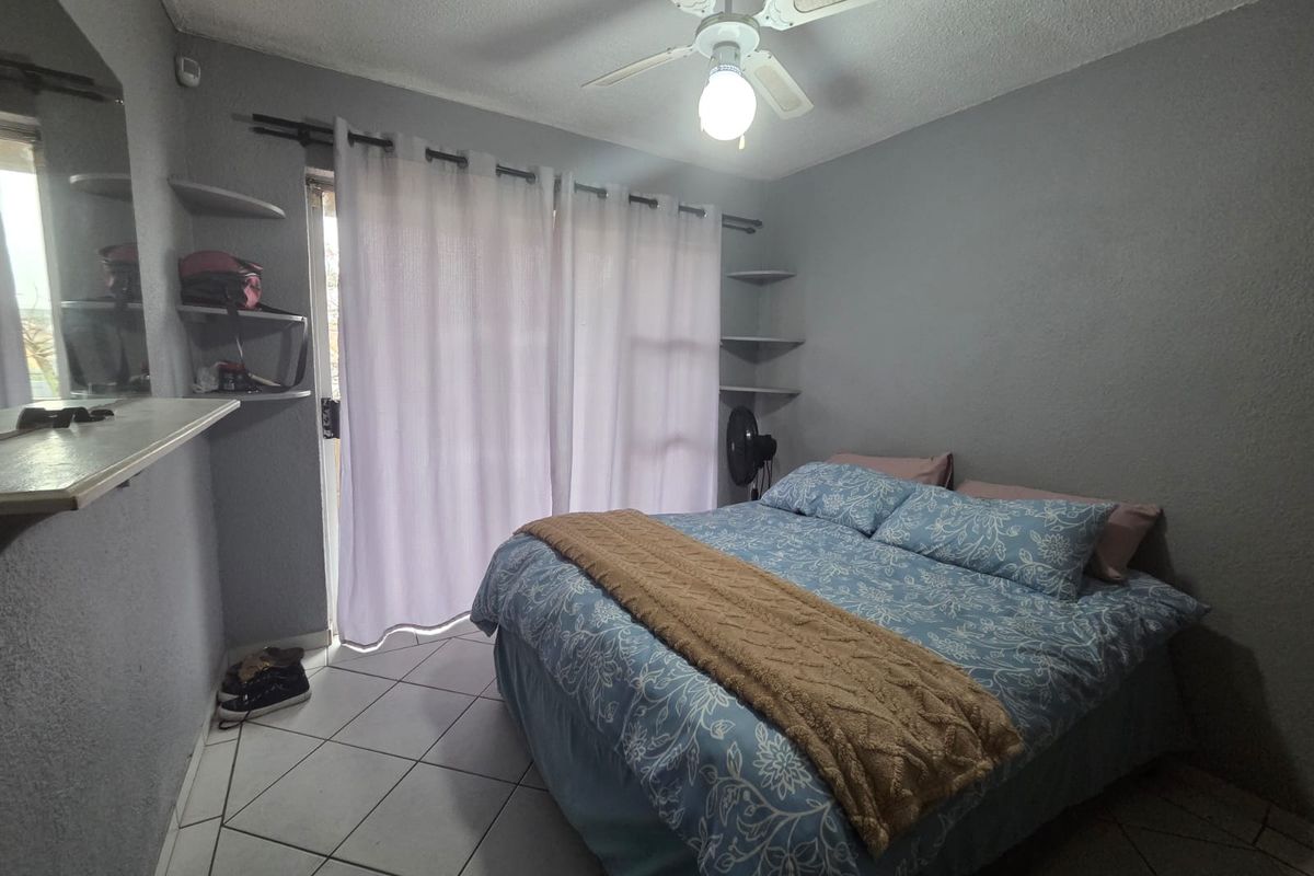 A bedroom featuring tiled flooring, a ceiling fan, and built-in shelving, with direct access to an outdoor area through a sliding glass door.
