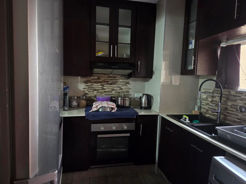 Compact kitchen featuring dark wood cabinetry, stone countertops, a mosaic tile backsplash, and integrated oven with extractor fan.