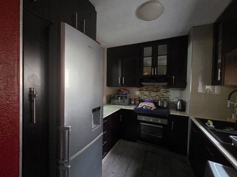 A compact kitchen featuring dark wood cabinetry, stone countertops, a built-in oven, and a tiled backsplash.