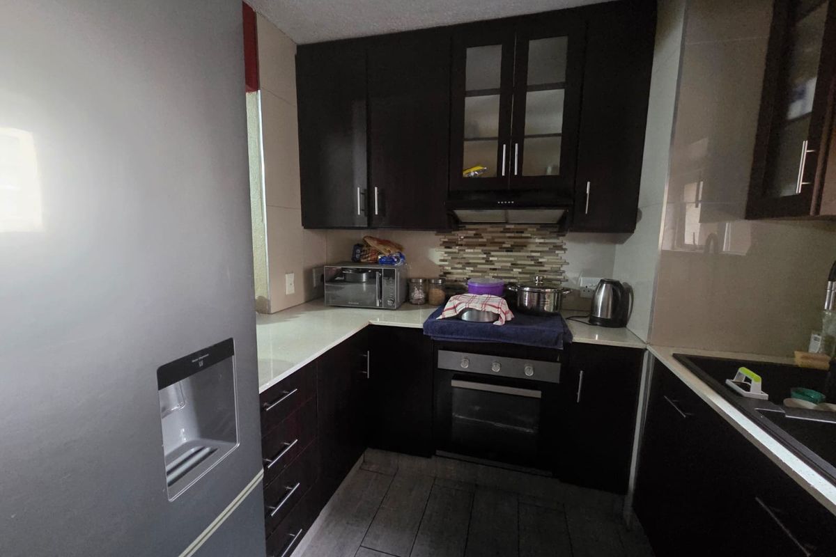 Compact kitchen featuring dark wood cabinetry, stone countertops, a built-in oven with extractor fan, and a tiled backsplash.