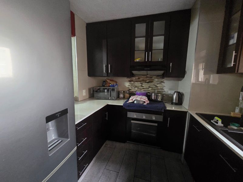 Compact kitchen featuring dark wood cabinetry, stone countertops, a built-in oven with extractor fan, and a tiled backsplash.
