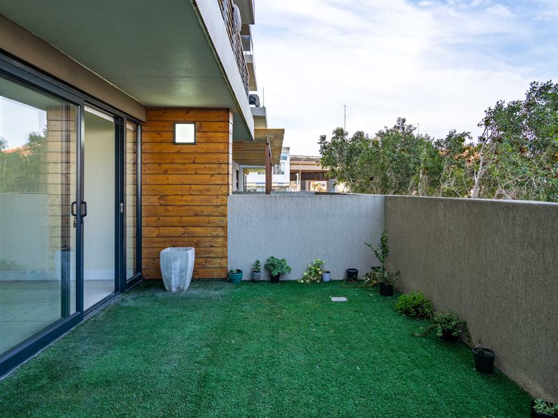 A private ground-floor patio featuring artificial turf, timber-clad accents, and sliding glass door access to the apartment interior.