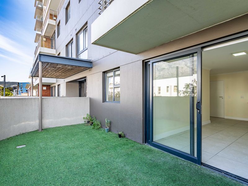 Ground floor apartment patio featuring artificial turf, a concrete boundary wall, and large sliding glass doors providing access to the interior living space.