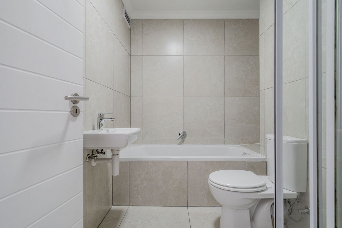 A clean, modern bathroom featuring neutral wall tiles, a built-in bathtub, a wall-mounted basin, and a standard toilet.