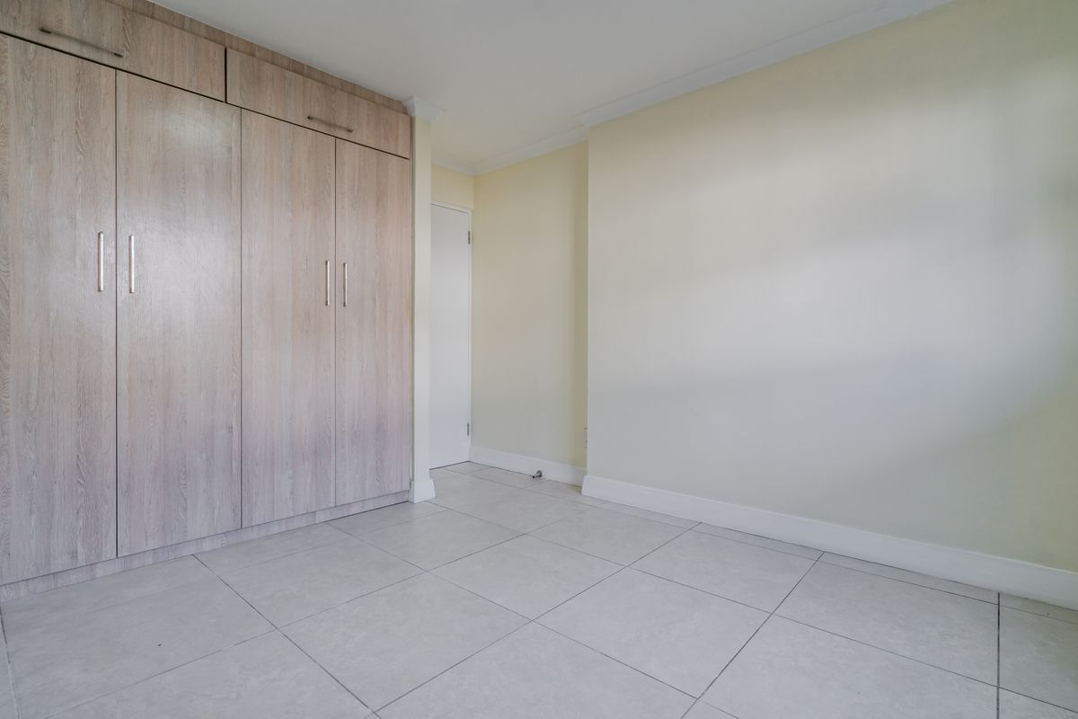 A clean, empty bedroom featuring light-toned built-in cupboards, neutral wall finishes, and modern tiled flooring.