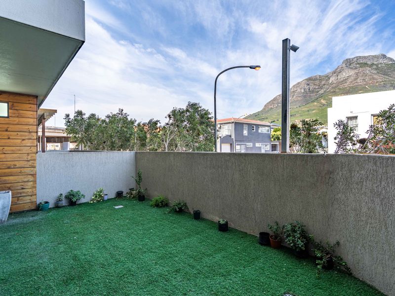 A private balcony area featuring artificial turf, timber wall cladding, and a textured boundary wall with mountain views.