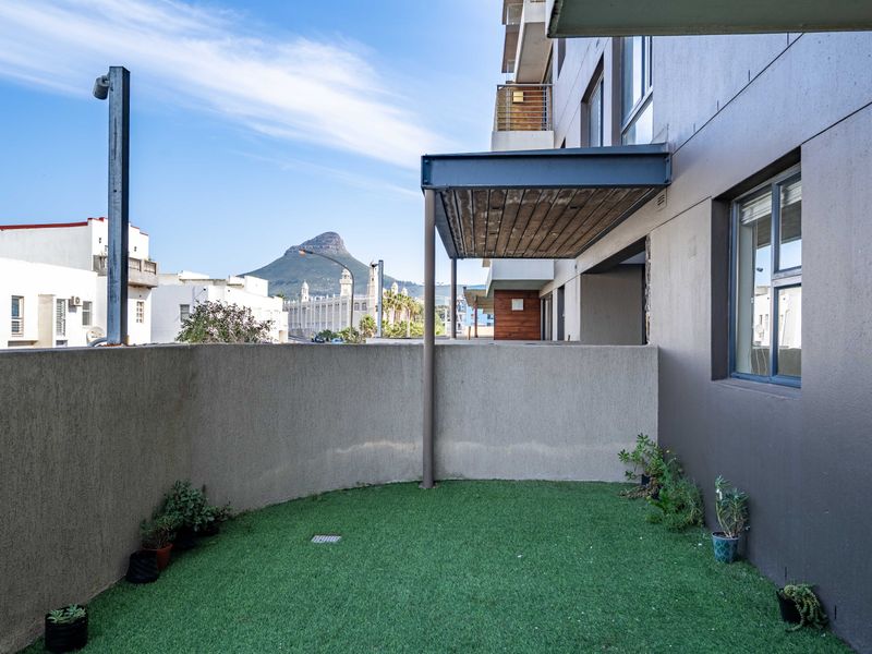 A private balcony area featuring artificial turf, a concrete boundary wall, and a metal pergola, offering an outdoor space with urban and mountain views.