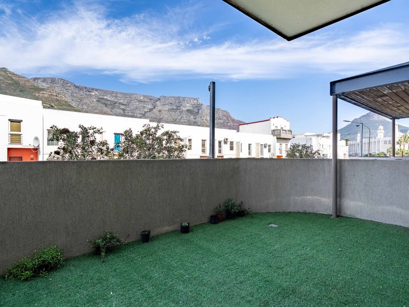 A private balcony area featuring artificial grass, a concrete boundary wall, and a metal pergola structure with scenic mountain views.