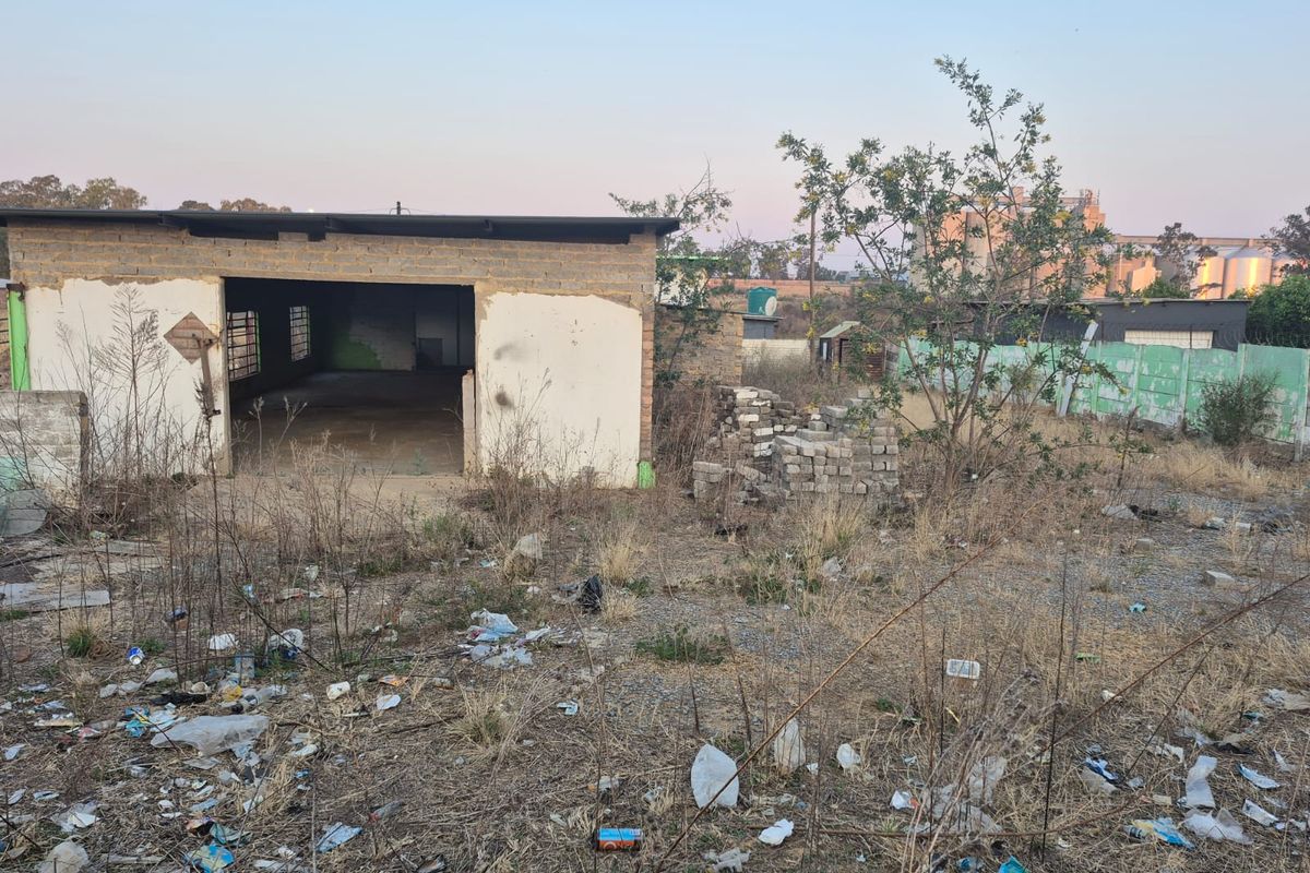 A view of a vacant residential plot featuring a dilapidated outbuilding structure and a precast concrete boundary wall, requiring significant site clearance and renovation.