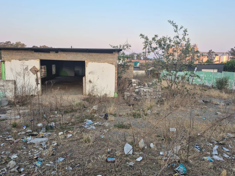 A view of a vacant residential plot featuring a dilapidated outbuilding structure and a precast concrete boundary wall, requiring significant site clearance and renovation.