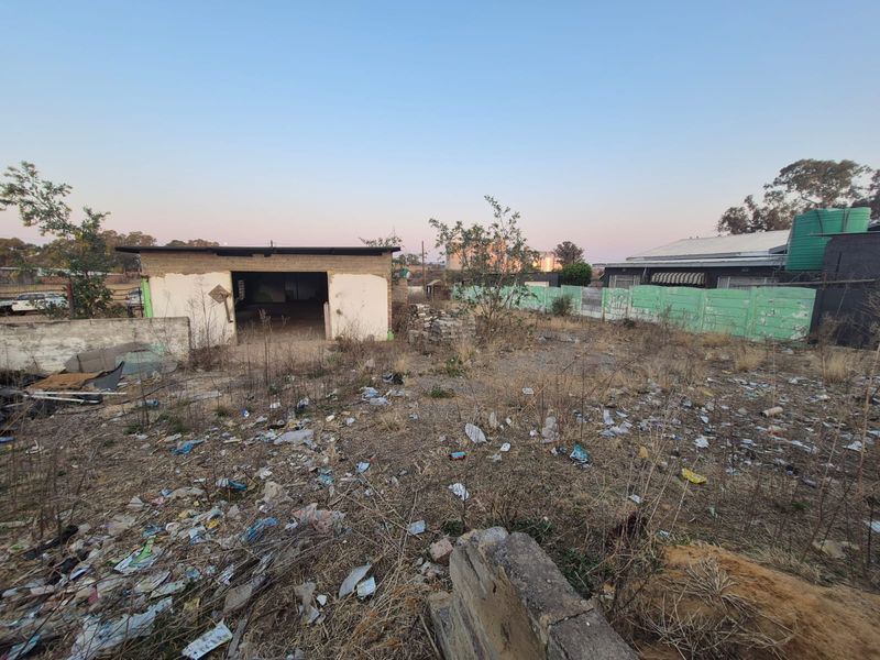 Vacant residential land featuring a detached garage structure, perimeter walling, and a water tank, currently requiring significant site clearing and maintenance.