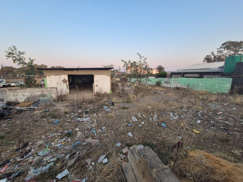 A vacant residential plot featuring a detached garage structure, perimeter walling, and a water tank, requiring significant clearing and maintenance.