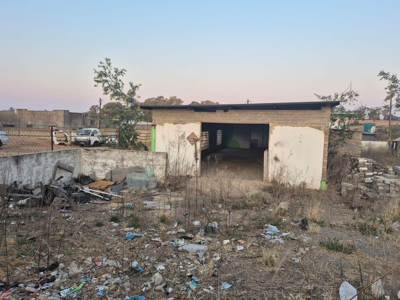 A view of a vacant residential plot featuring a small, unfinished brick structure and significant debris on the property grounds.