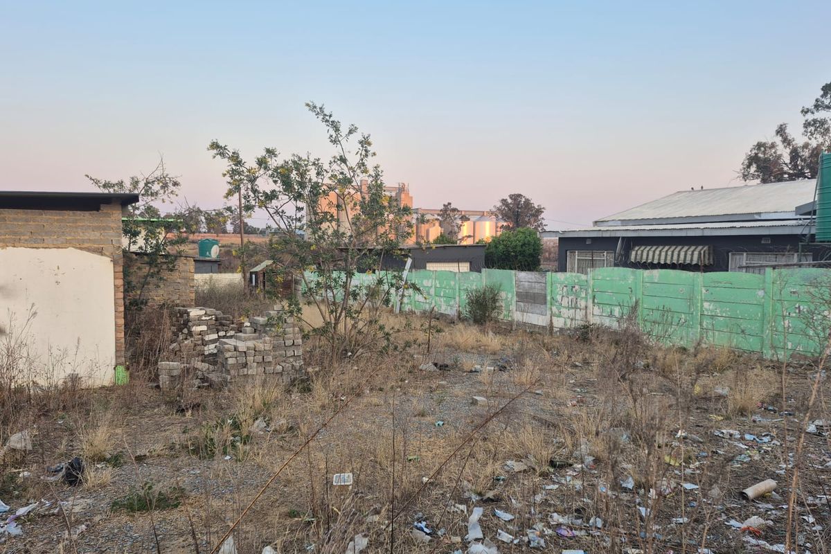 A vacant residential plot featuring a precast concrete boundary wall, water tank, and significant overgrown vegetation with accumulated debris.