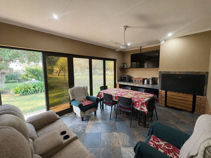 Spacious covered patio featuring a built-in braai, tiled flooring, ceiling fan, and large sliding glass doors providing direct access to the garden.