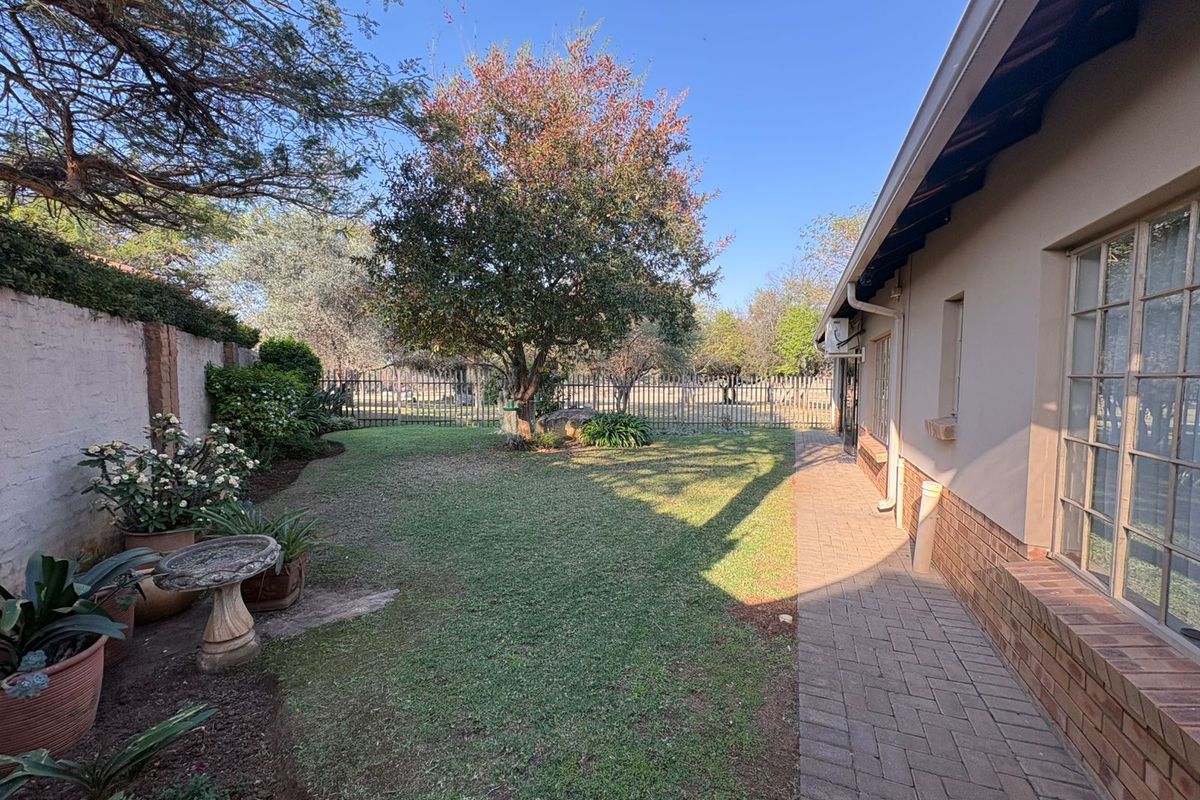 A well-maintained rear garden featuring a brick-paved walkway, established lawn, mature tree, and secure perimeter fencing.