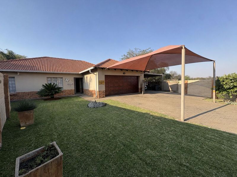 Front view of a well-maintained house featuring a tiled roof, brick accents, a paved driveway with a shade sail, and a neat front lawn.
