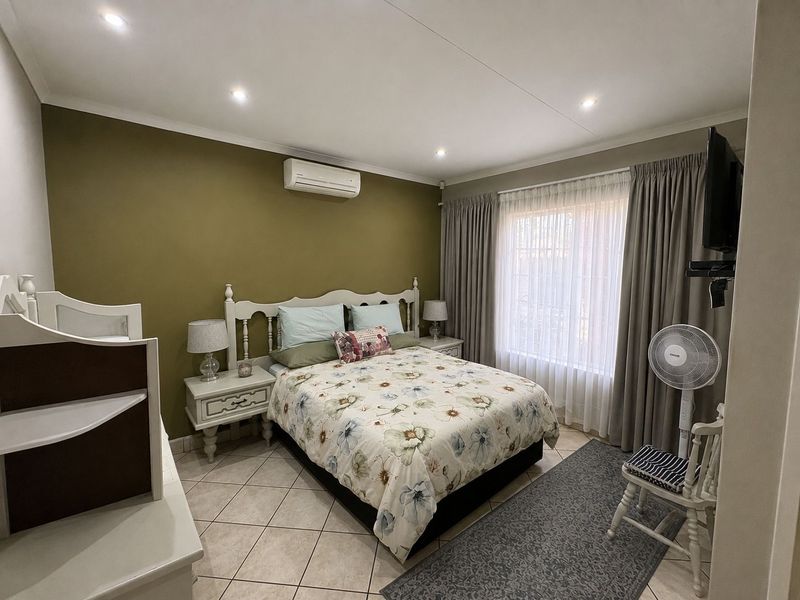 A well-maintained bedroom featuring tiled flooring, recessed downlighting, and a wall-mounted split-system air conditioning unit.