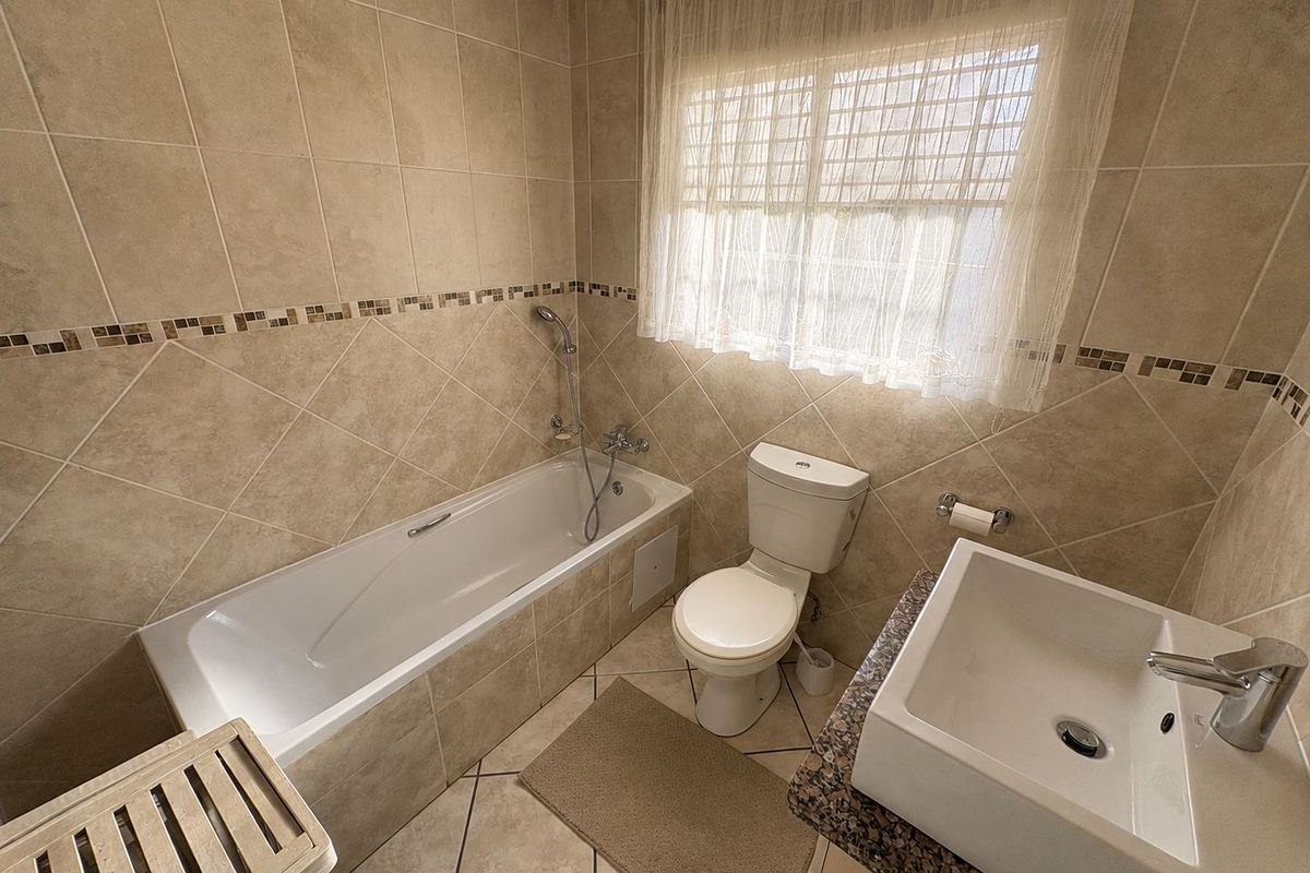 A clean, neutral-toned bathroom featuring a tiled bathtub, a modern basin with a granite vanity top, and a standard toilet.