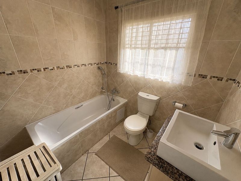 A clean, neutral-toned bathroom featuring a tiled bathtub, a modern basin with a granite vanity top, and a standard toilet.