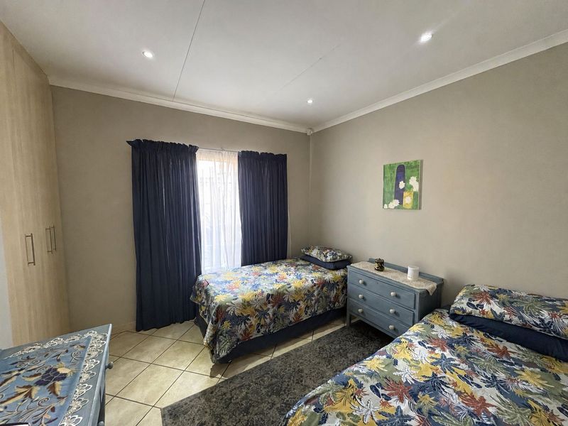 A well-maintained bedroom featuring neutral wall tones, tiled flooring, recessed downlighting, and built-in storage cupboards.